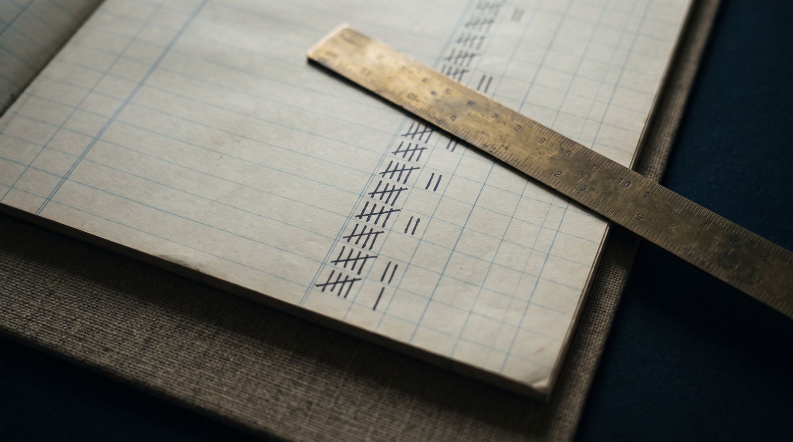 An open ledger page with ruled columns and a brass ruler laid across it.